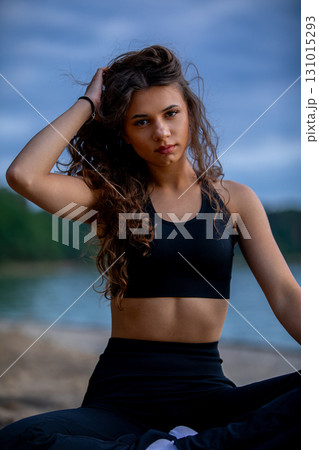A Young Woman in Stylish Athletic Wear Posing by a Calm and Beautiful Body of Water 131015293