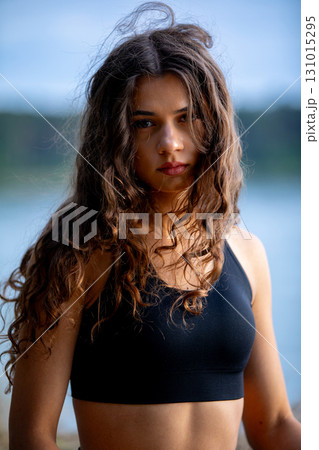 A young woman enjoys her time by the water, showcasing her long hair while dressed in sporty attire A young woman enjoys her time by the water, showcasing her long hair while dressed in sporty attire 131015295