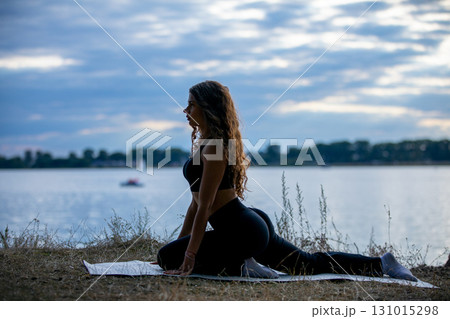 A Woman Practicing Yoga by a Serene and Tranquil Lake During the Beautiful Sunset Hour A Woman Practicing Yoga by a Serene and Tranquil Lake During the Beautiful Sunset Hour 131015298