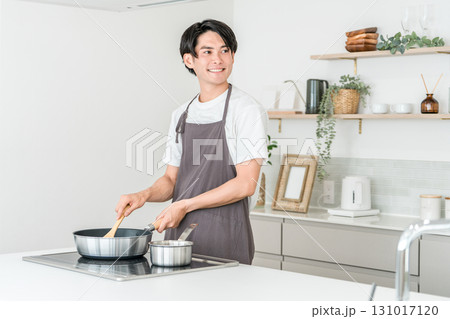 キッチンのIHコンロでフライパンを使い痛め料理をするエプロン姿の若いアジア人男性 131017120