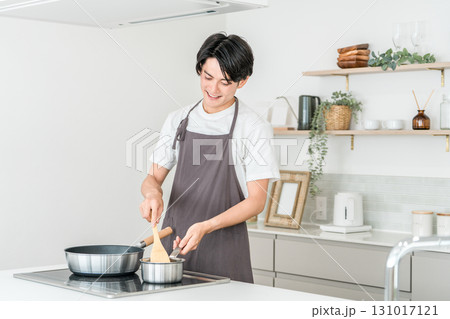 キッチンのIHコンロでフライパンを使い痛め料理をするエプロン姿の若いアジア人男性 131017121