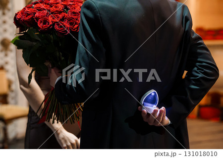 Romantic Proposal with Red Roses and Ring Box: Man Offering Engagement Ring to Woman in Dark Venue 131018010