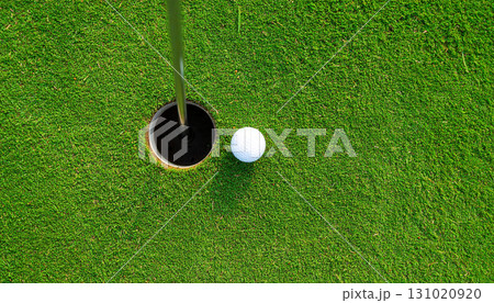 Golf ball green grass putting hole overhead view crucial putt pristine surface close up outdoor sport competition. Aerial perspective captures tense moment as white golf ball nears hole vibrant 131020920
