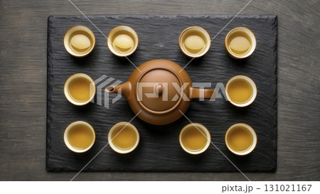 Traditional tea ceremony setup with a teapot and cups arranged on a dark slate tray 131021167