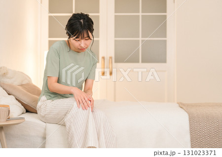 夜のベッドルームで膝を痛がる若いアジア人女性 夜のベッドルームで膝を痛がる若いアジア人女性 131023371