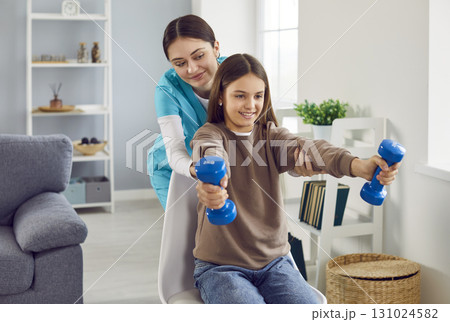 Child girl doing exercise using dumbbells with support from a young friendly female nurse. Child girl doing exercise using dumbbells with support from a young friendly female nurse. 131024582