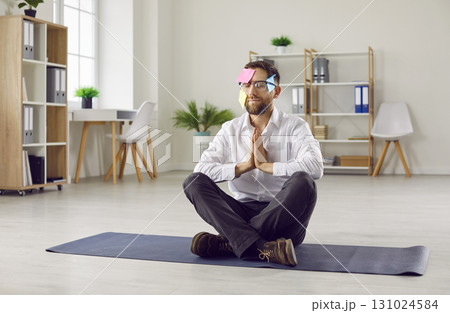 Funny relaxed business man meditating in office or at home sitting on the floor on yoga mat. 131024584