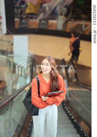 Young professional woman with laptop on escalator, symbolizing business lifestyle, confidence, mobility, and modern career success in an urban environment Young professional woman with laptop on escalator, symbolizing business lifestyle, confidence, mobility, and modern career success in an urban environment 131025840