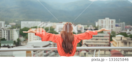 A businesswoman on a rooftop terrace, arms open, enjoying a refreshing break with city and mountain views A businesswoman on a rooftop terrace, arms open, enjoying a refreshing break with city and mountain views 131025846