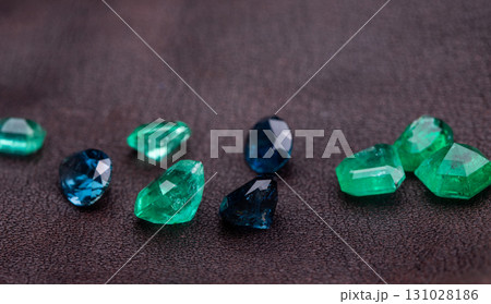 A collection of green, blue, and red gemstones are displayed on a dark surface A collection of green, blue, and red gemstones are displayed on a dark surface 131028186