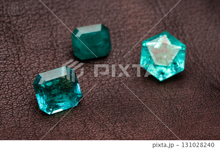 Three green gemstones are on a brown surface Three green gemstones are on a brown surface 131028240