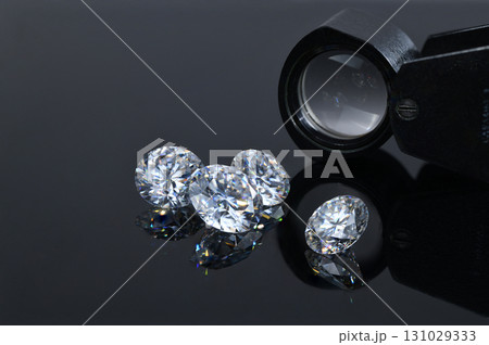 Three diamonds are on a table next to a magnifying glass 131029333