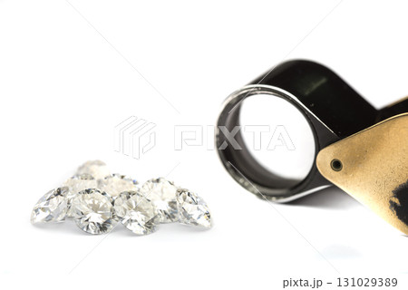 A close up of a magnifying glass with a pile of diamonds on a white background 131029389