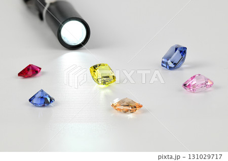 A flashlight is shining on a table with a variety of colored gems 131029717