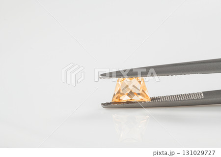 A small yellow gemstone is held in a pair of tweezers 131029727
