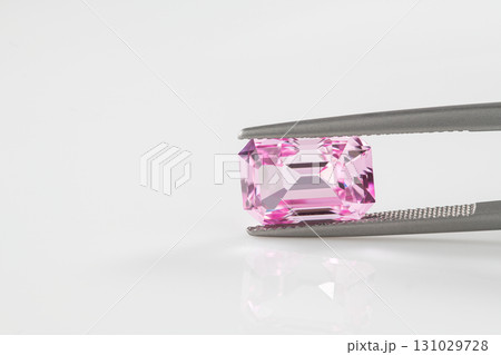 A pink gemstone is being held in a metal clamp 131029728