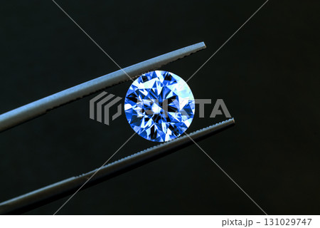 A blue diamond is being held up by a pair of tweezers 131029747
