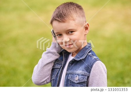 Caucasian young male child smiling outdoors in denim vest talking on smartphone Caucasian young male child smiling outdoors in denim vest talking on smartphone 131031353