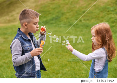 Young caucasian boy and girl blowing bubbles in a green park setting 131031492