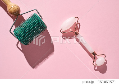 Facial massage tools on pink background: jade roller and microneedle Facial massage tools on pink background: jade roller and microneedle 131031571
