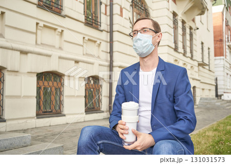Caucasian young adult male in mask and blue blazer holding coffee outdoors Caucasian young adult male in mask and blue blazer holding coffee outdoors 131031573