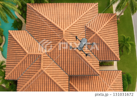 Aerial view of drone performing roof inspection over tiled rooftops surrounded by palm trees. concept of technology in construction, drone inspection, modern roofing solutions 131031672