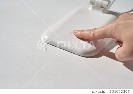 Close-up of a finger touching white wireless charging pad on white background Close-up of a finger touching white wireless charging pad on white background 131032397