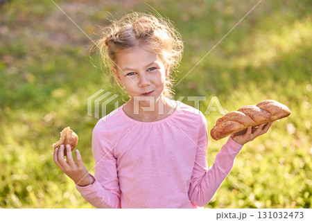 Caucasian child enjoying fresh bread outdoors with sunlit background in park 131032473