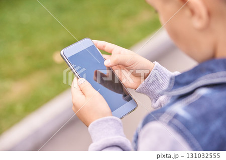 Young caucasian male child using smartphone outdoors in a denim jacket Young caucasian male child using smartphone outdoors in a denim jacket 131032555