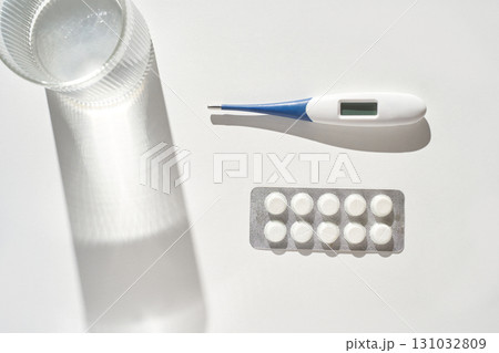 Digital thermometer, glass of water, and blister pack of pills on white surface Digital thermometer, glass of water, and blister pack of pills on white surface 131032809