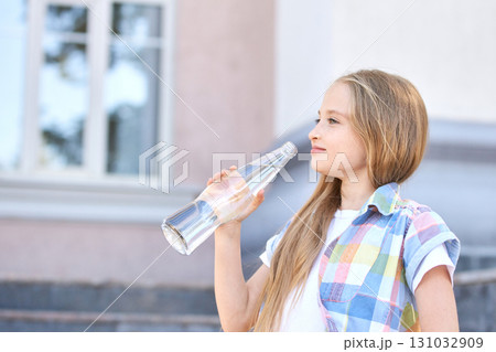 Young caucasian girl drinking water outdoors with a clear bottle on a sunny day Young caucasian girl drinking water outdoors with a clear bottle on a sunny day 131032909