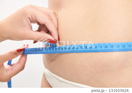 Female measuring waist with blue tape measure for fitness and health goals Female measuring waist with blue tape measure for fitness and health goals 131033026