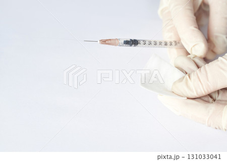 Hands in gloves holding syringe with cotton pad on white background for medical 131033041