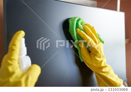 Person cleaning screen with green cloth and yellow gloves spray bottle indoors 131033069