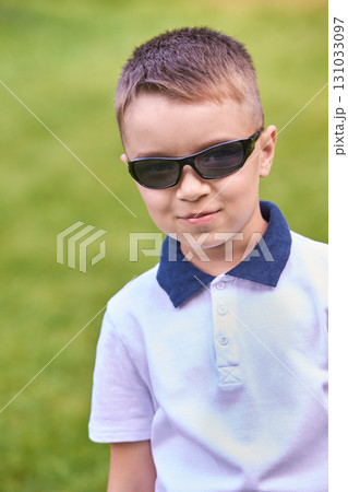 Caucasian young male child wearing sunglasses smiling outdoors in green park Caucasian young male child wearing sunglasses smiling outdoors in green park 131033097