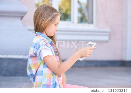 Caucasian young girl using smartphone outdoors with long blonde hair wearing 131033215