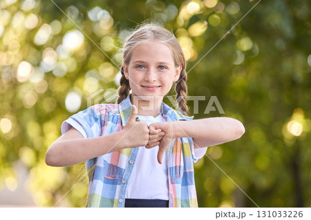 Blonde caucasian girl giving thumbs up and down outdoors in colorful shirt 131033226