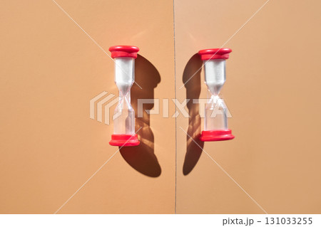 Symmetrical red hourglasses on beige background with shadows reflecting time Symmetrical red hourglasses on beige background with shadows reflecting time 131033255