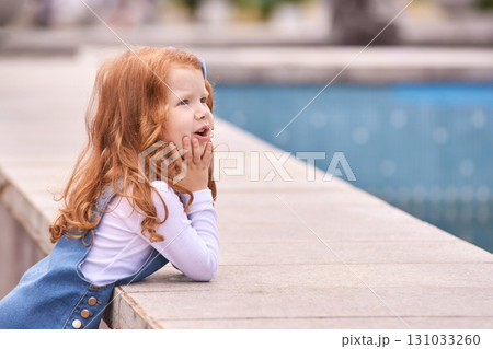 Curious caucasian young girl with red hair contemplating near a pool in outdoor Curious caucasian young girl with red hair contemplating near a pool in outdoor 131033260