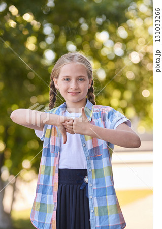 Caucasian young girl outdoors with braided hair making thumbs up and down Caucasian young girl outdoors with braided hair making thumbs up and down 131033266