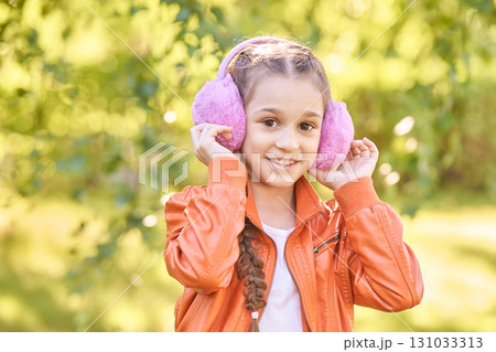 Smiling young caucasian girl wearing pink earmuffs outdoors in bright orange Smiling young caucasian girl wearing pink earmuffs outdoors in bright orange 131033313