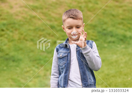 Caucasian young male child blowing soap bubbles outdoors in denim jacket 131033324