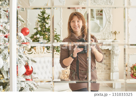 Young caucasian female photographer reflecting in mirror with christmas tree 131033325