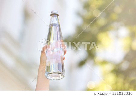Hand holding glass bottle with fresh water outdoors on sunny day Hand holding glass bottle with fresh water outdoors on sunny day 131033330
