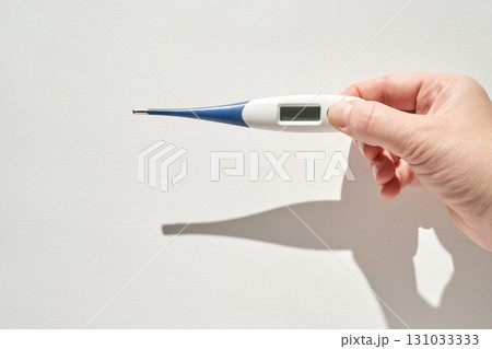 Caucasian adult hand holding digital thermometer against white background 131033333