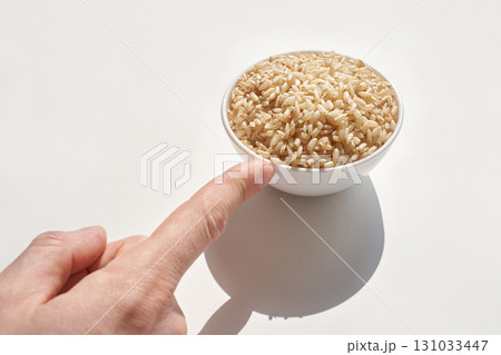 Hand pointing to bowl of uncooked brown rice on white background highlighting Hand pointing to bowl of uncooked brown rice on white background highlighting 131033447
