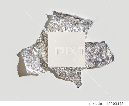 Blank square card on crumpled aluminum foil against light gray background Blank square card on crumpled aluminum foil against light gray background 131033454