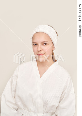 Young caucasian female in white bathrobe and headband smiling confidently Young caucasian female in white bathrobe and headband smiling confidently 131033479