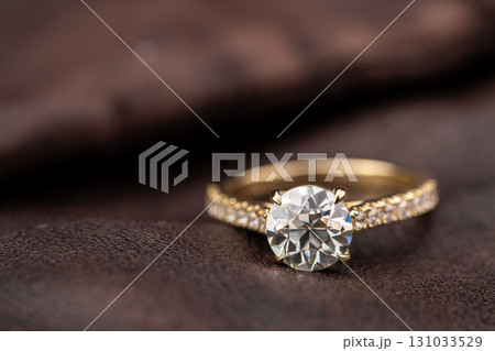 A gold and white diamond ring sits on a brown surface 131033529