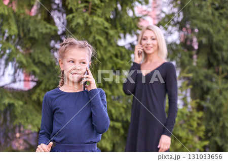 Caucasian child and adult female using smartphones in outdoor park setting 131033656